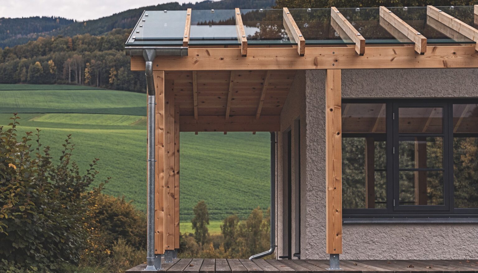 Terrassenüberdachung aus Holz mit Glaseindeckung und Dachrinne an einem Einfamilienhaus im Waldviertel